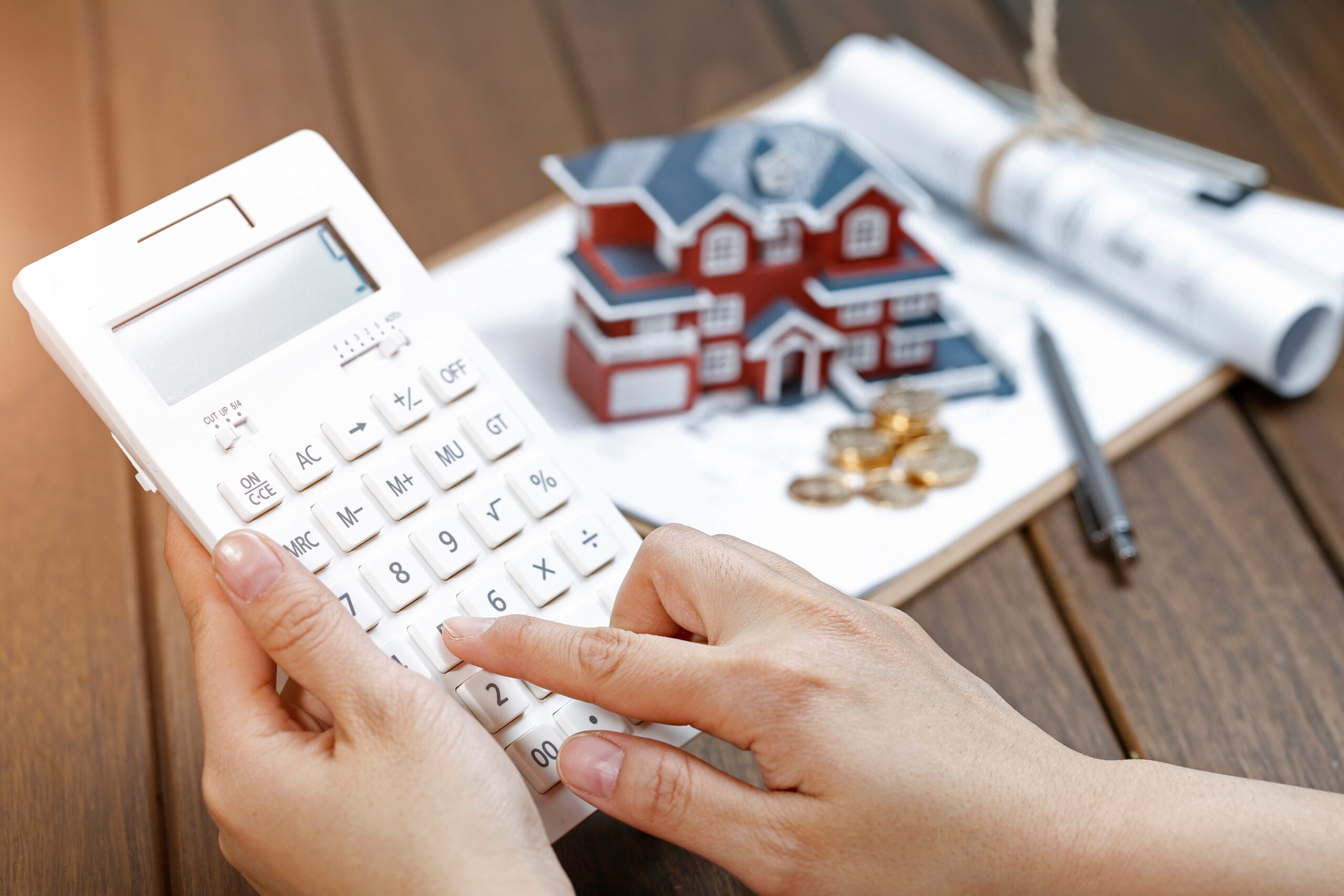 A female hand operating a calculator in front of a Villa house model A female hand operating a calculator in front of a Villa house model